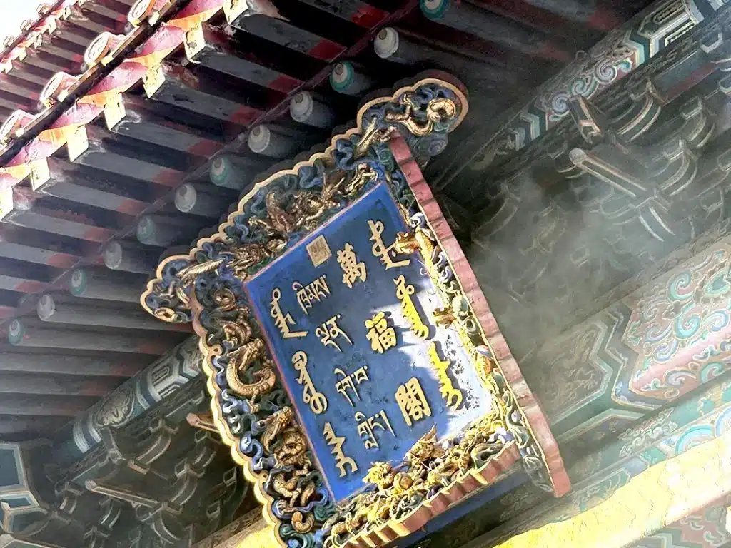 Ornate plaque and traditional wooden roof beams at the main entrance of Yonghe Temple in Beijing, China.