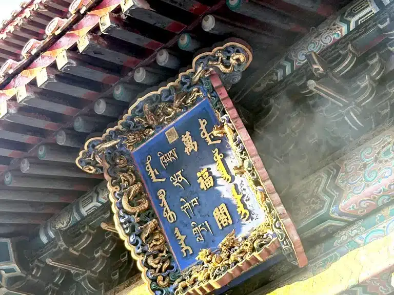 Ornate plaque and traditional wooden roof beams at the main entrance of Yonghe Temple in Beijing, China.