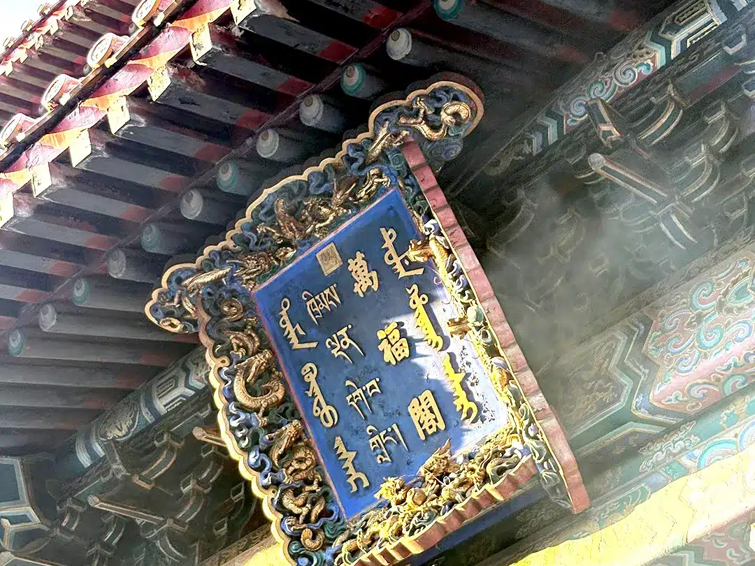 Ornate plaque and traditional wooden roof beams at the main entrance of Yonghe Temple in Beijing, China.
