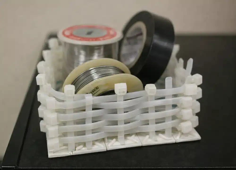 Cable ties woven into a small storage basket holding tape and solder wire spools