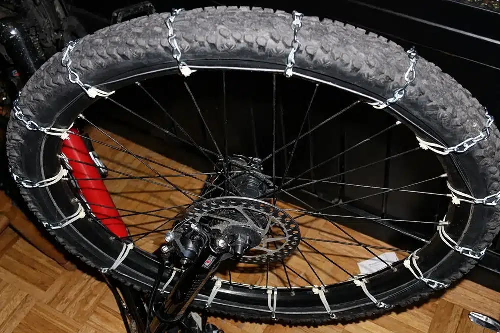 Nylon cable ties securing metal chains on a bicycle tire to create a DIY snow traction setup