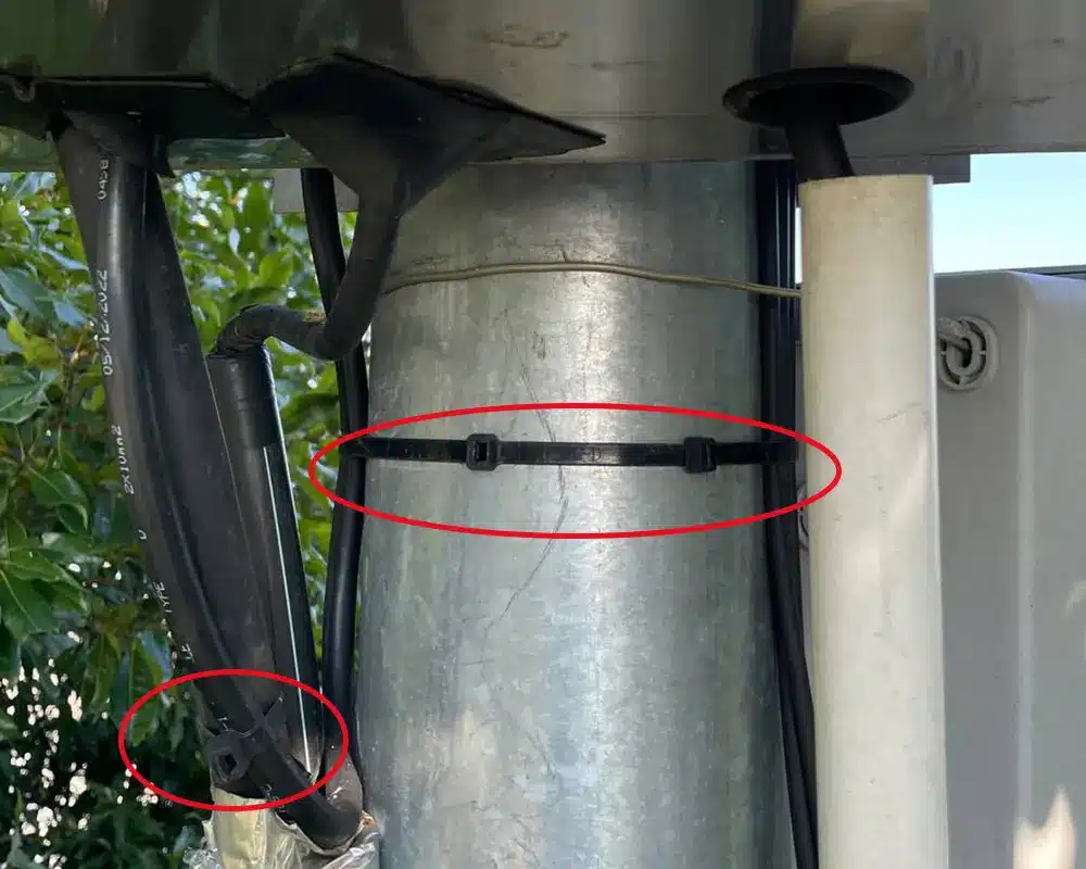 Black cable ties used to secure electrical cables to a metal pole in an outdoor installation