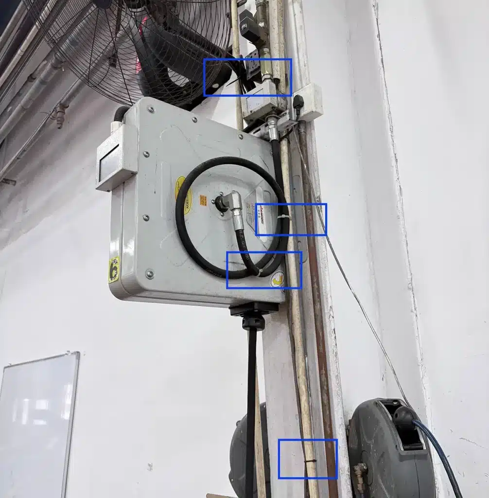 Cable ties highlighted in blue boxes securing hoses and cables around a wall-mounted reel and vertical pipework in a BMW service bay