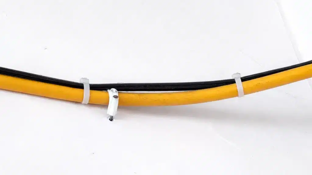 Cable clips and cable ties securing black and yellow cables along a wall