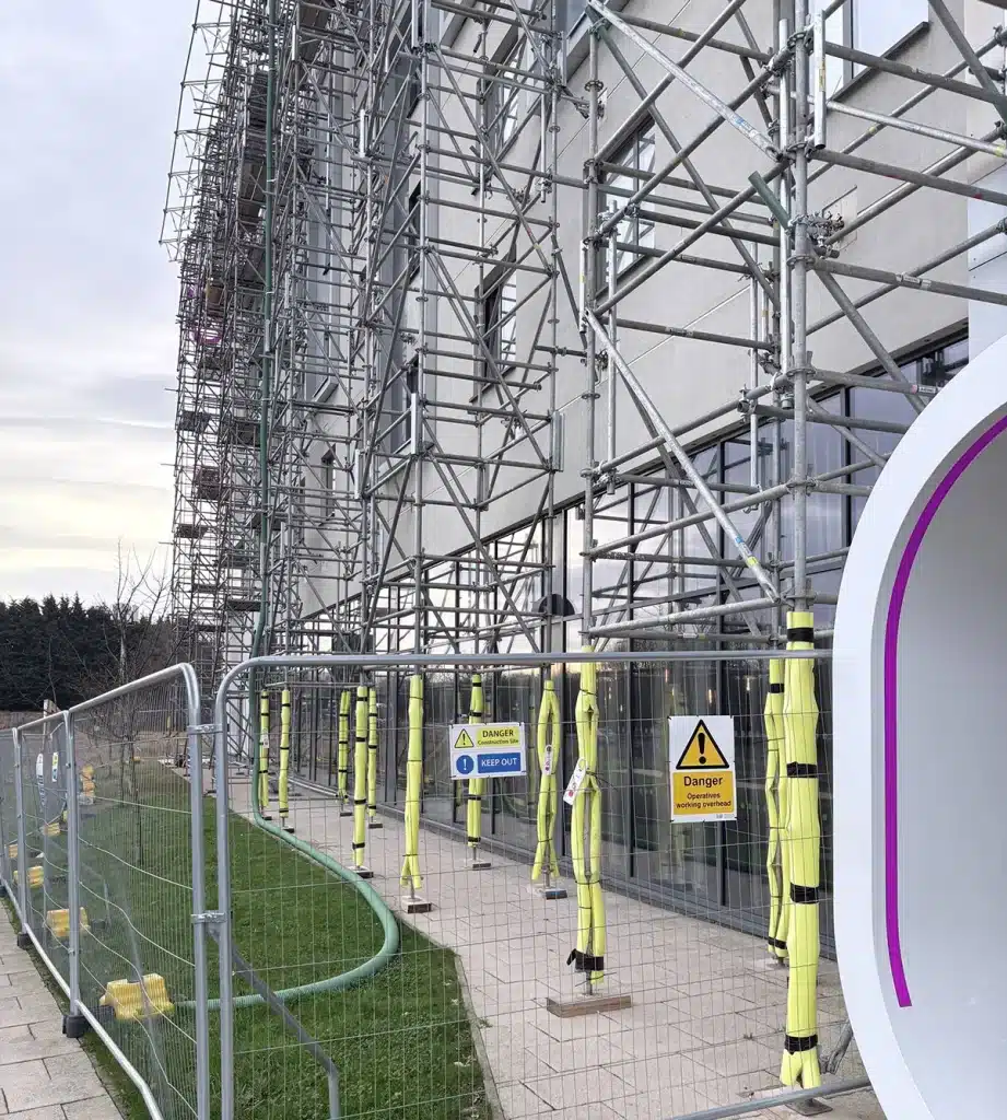 Cable ties securing yellow foam padding and safety signs on temporary site fencing in Germany.