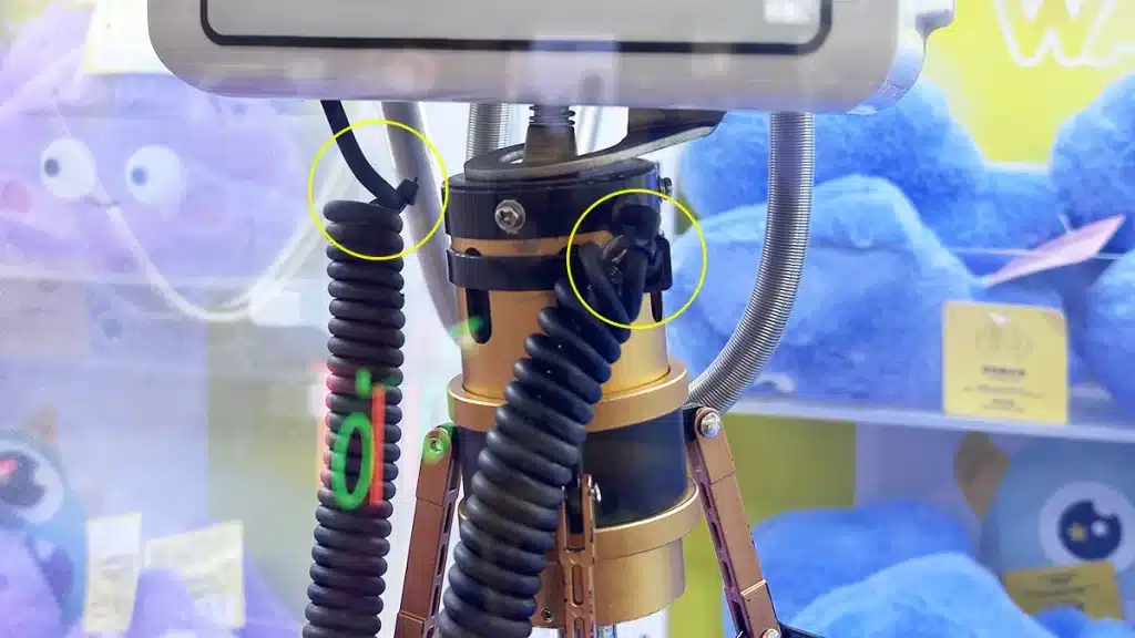 Nylon cable ties securing black wires near the grabber motor of a claw machine